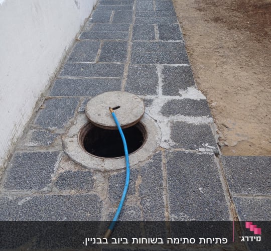 צינור כחול מחובר לפתח ביוב פתוח על מדרכה